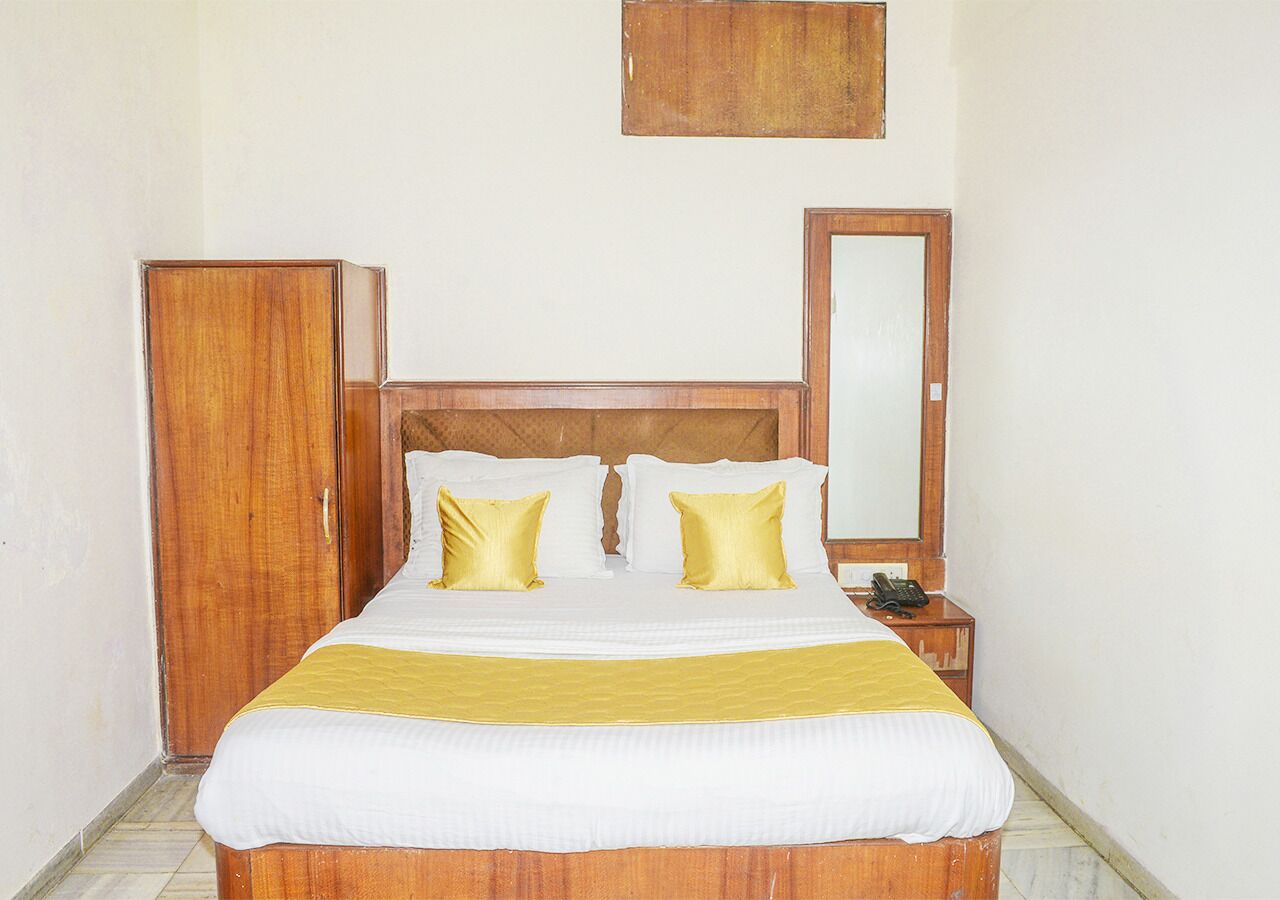 A standard hotel room with a wooden bed, two pillows, a bedside table with a phone, and a wardrobe.