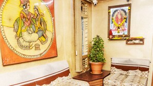 A room with a sofa, a potted plant, a framed picture, and a small shelf with items. - Hotel Subhash (Mumbai)