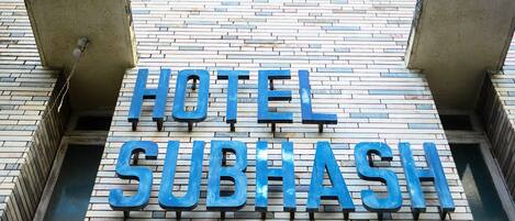 Een bord met daarop HOTEL SUBHASH, met een modern ontwerp en een bakstenen gevel.