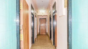 A narrow hallway with wooden doors on both sides, a tiled floor, and a plain ceiling. - Hotel Subhash (Mumbai)