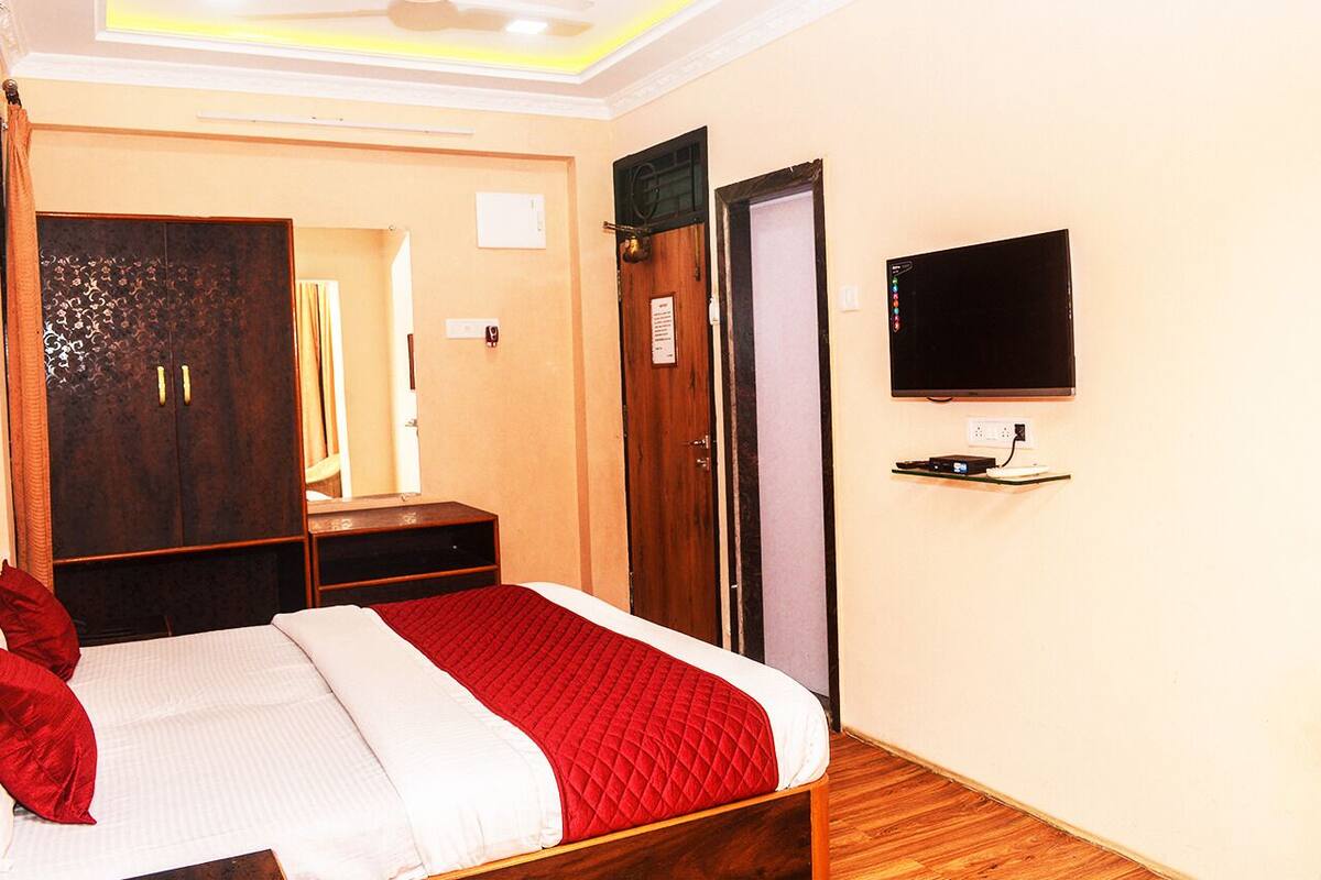 A hotel room with a bed, a TV mounted on the wall, a wooden wardrobe, and a door.