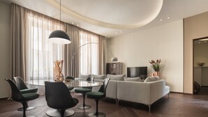 A modern living room with a round dining table, green upholstered chairs, a grey sofa, and a flat-screen TV. - Sant'Ambrogio Luxury Apartment R&R (Milano)