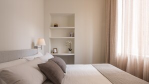 A neatly arranged hotel room with a bed, bedside table, lamp, and a shelf with decorative items. - Sant'Ambrogio Luxury Apartment R&R (Milano)