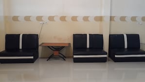 Een wachtruimte met drie zwarte stoelen met witte strepen, een kleine tafel en een muur met een ruitpatroon.