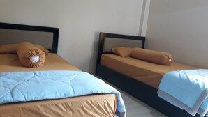 Twee enkele bedden met zwarte hoofdborden, beige beddengoed en een lichtblauwe deken.