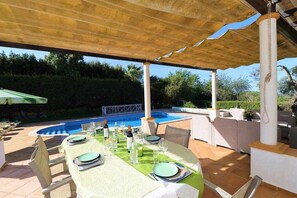Un espace extérieur aménagé pour les repas, avec une piscine, une pergola et de nombreuses plantes.