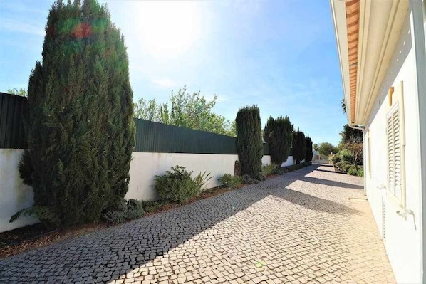 A cobblestone pathway leading to a building with a white facade and a green roof.