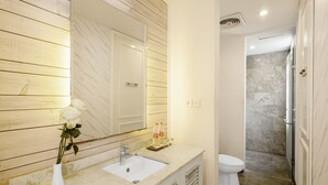 A bathroom with a wooden wall, a white sink, a mirror, and a shower area. - The Kanjeng Suites Petitenget (Keroboken Kelod)