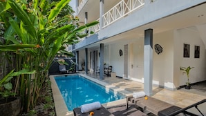 A poolside area with lounge chairs, a dining table, and potted plants. - The Kanjeng Suites Petitenget (Keroboken Kelod)
