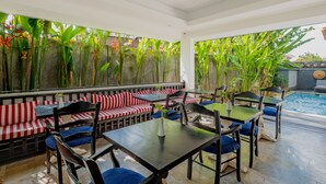 An outdoor dining area with red and white striped benches, black tables, and blue cushioned chairs. - The Kanjeng Suites Petitenget (Keroboken Kelod)