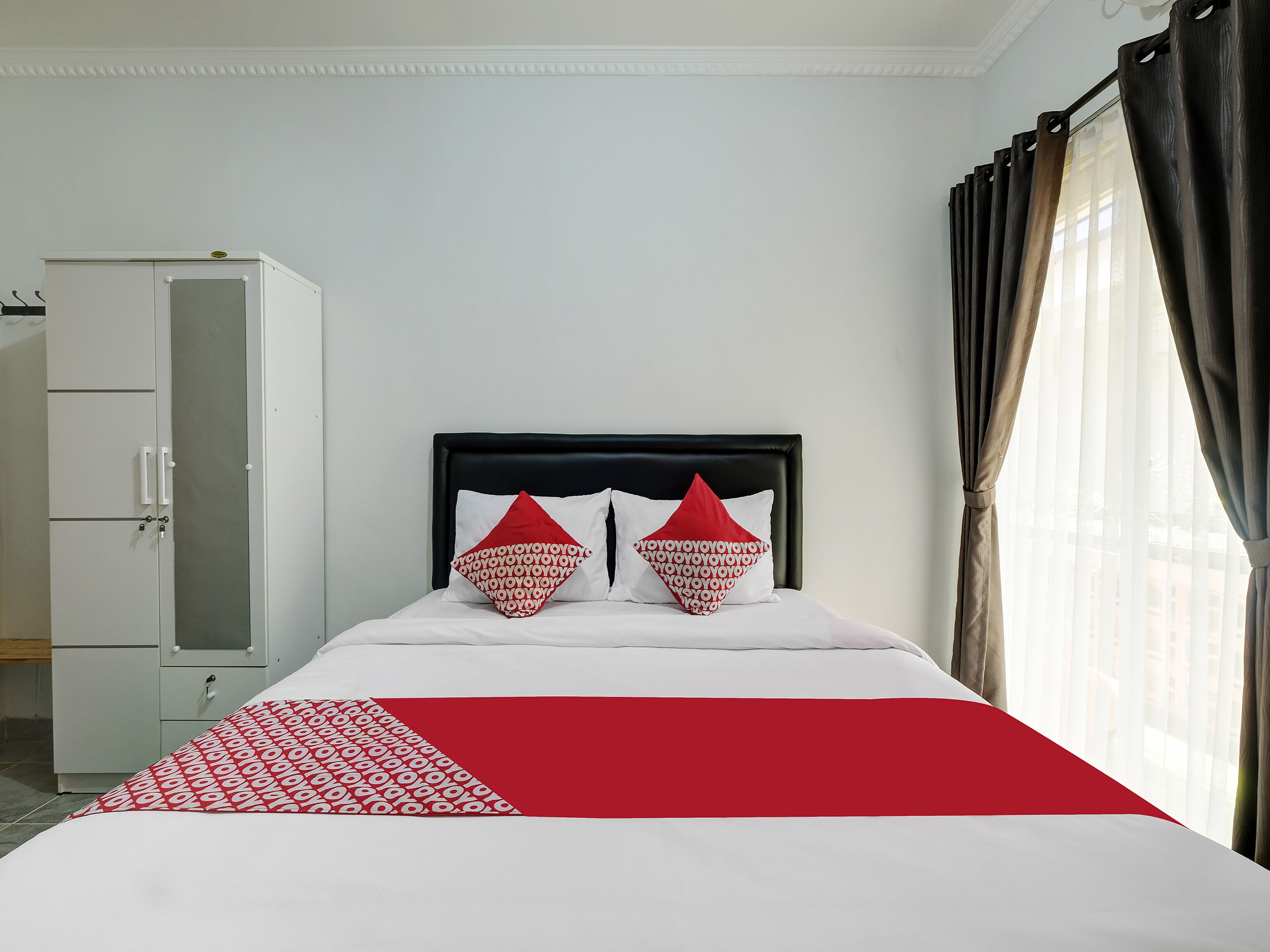 A hotel room with a bed, two pillows, a wardrobe, and a window with curtains.