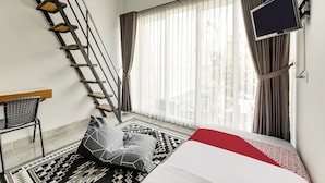 A modern hotel room with a bed, a flat-screen TV, a desk, and a staircase. - Capital O 90983 Harmony Easy Stay (Depok)