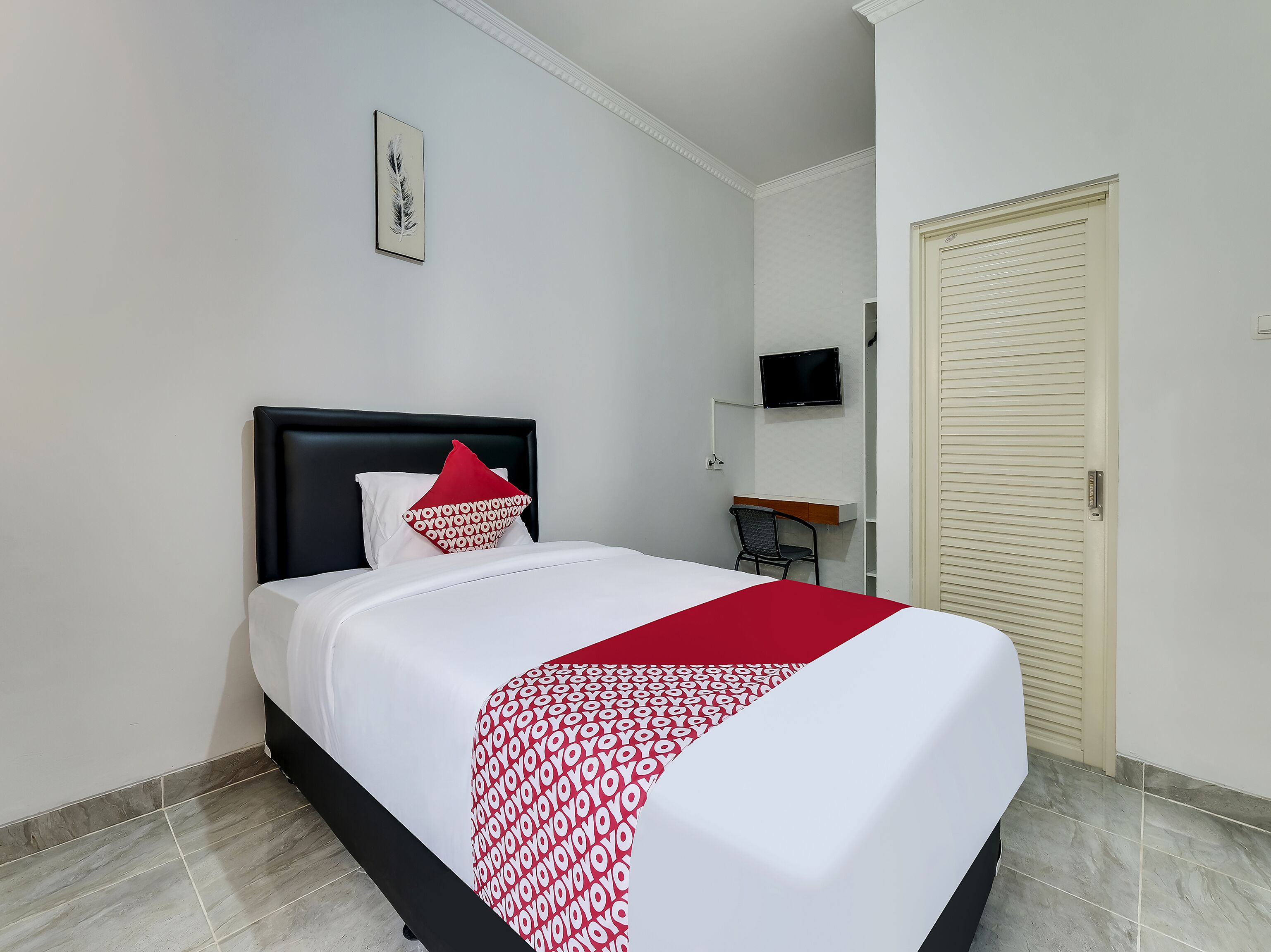 Un lit bien fait, avec une couverture à motifs, un oreiller rouge et une tête de lit noire.