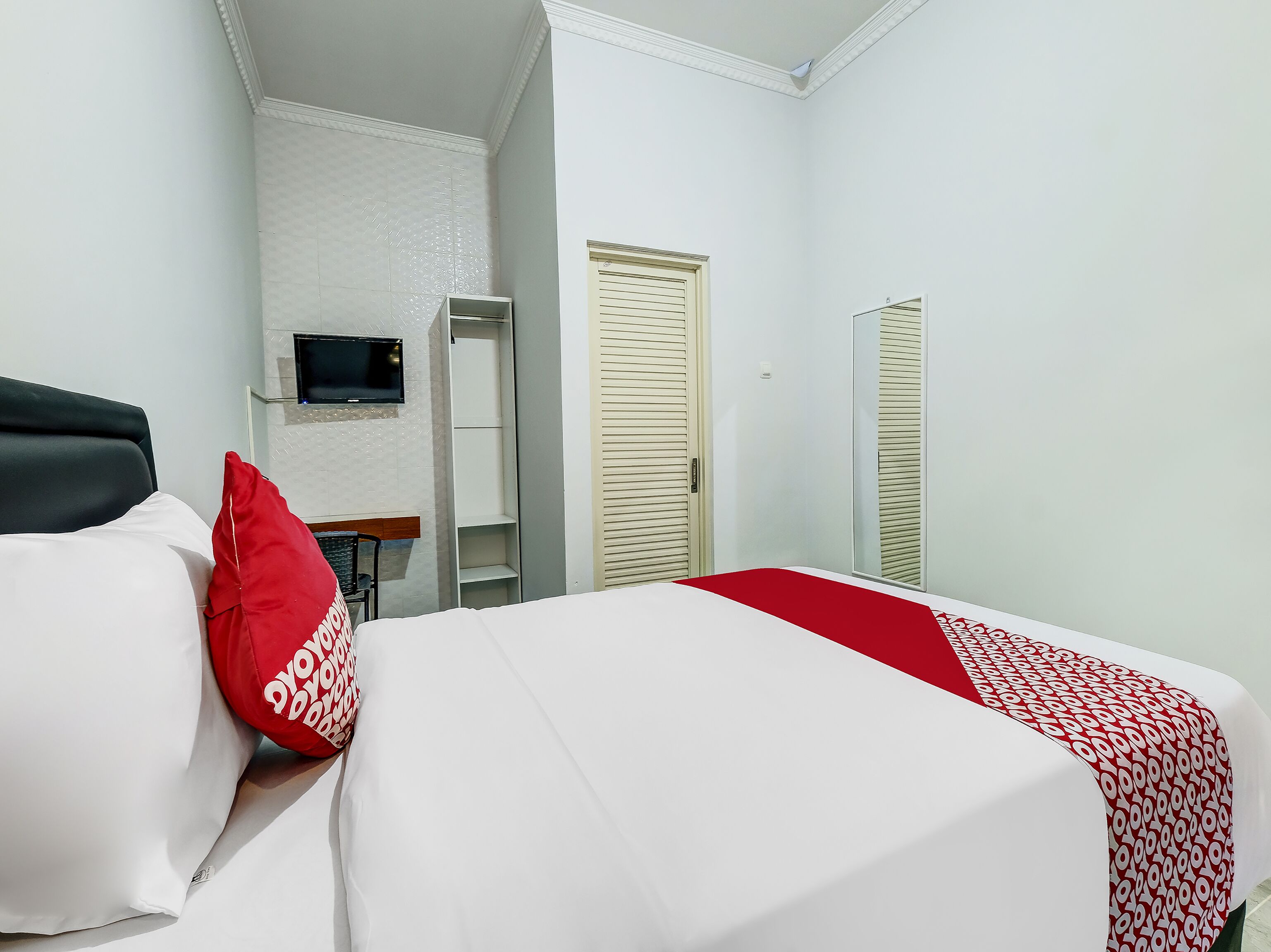 A hotel room with a bed, a TV mounted on the wall, a wardrobe, and a mirror.