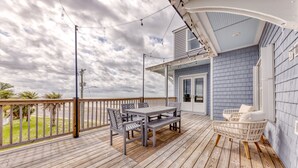 A wooden deck with a table and chairs, a wicker chair, and a view of the ocean. - Beachfront |Cargo Elevator | Steps to Beach | Baby+Beach Gear | Lawn+Board Games (Long Beach)