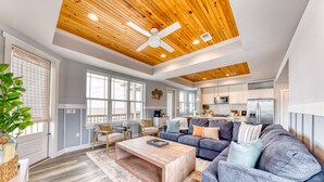 A spacious living room with a large gray sofa, wooden coffee table, and a ceiling fan. - Beachfront |Cargo Elevator | Steps to Beach | Baby+Beach Gear | Lawn+Board Games (Long Beach)