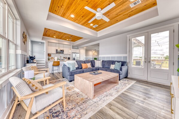A spacious living room with a large sofa, a coffee table, and a view of the backyard through a sliding door. - Beachfront |Cargo Elevator | Steps to Beach | Baby+Beach Gear | Lawn+Board Games (Long Beach)