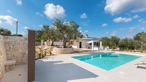 Un área de piscina con un muro de piedra, una pérgola y un edificio al fondo.