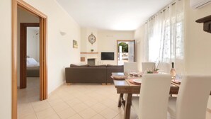 Una sala de estar con un sofá, una mesa de comedor dispuesta con platos y vasos, y un televisor montado en la pared.