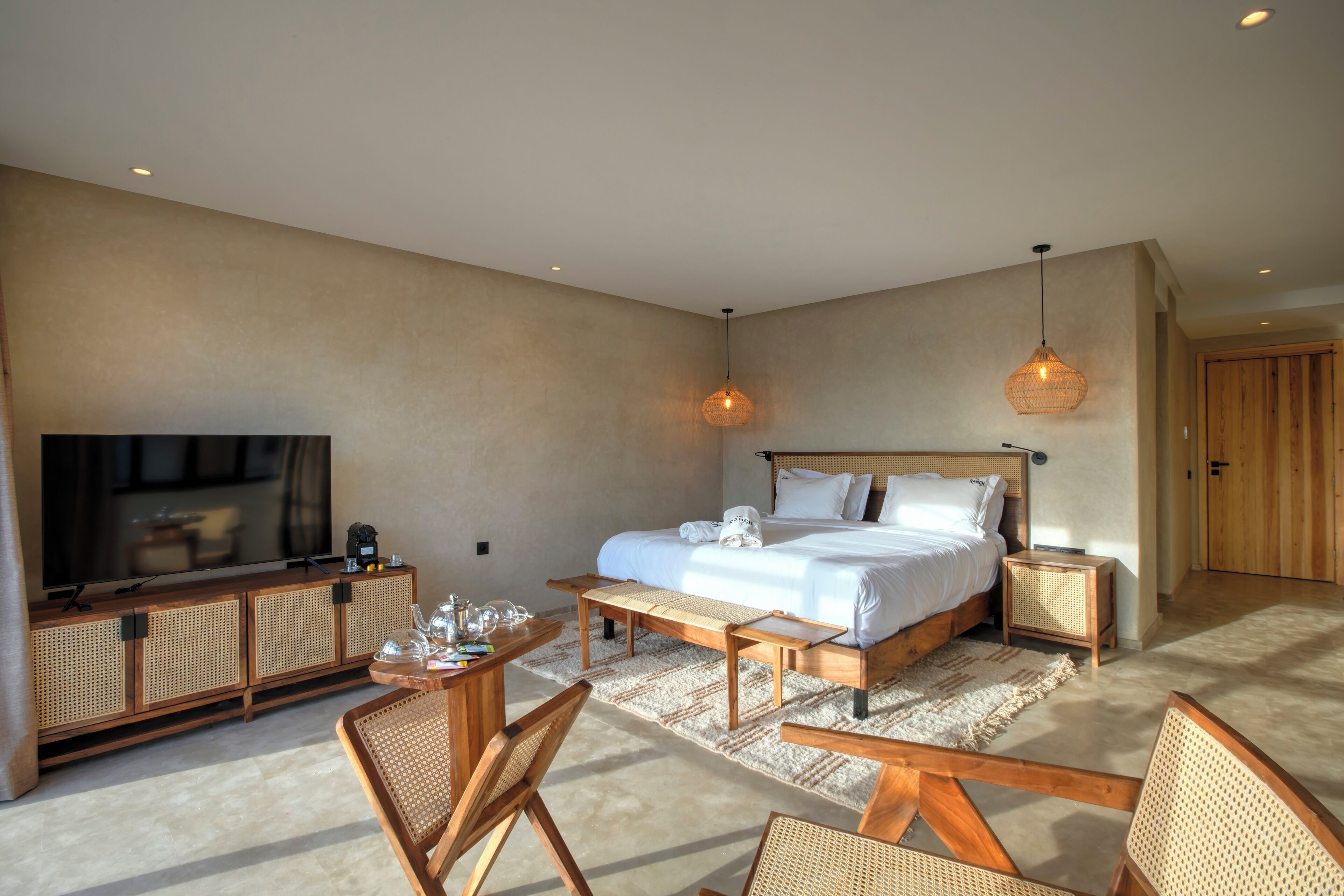 Une chambre spacieuse avec un grand lit, une télévision, une console en bois et un coin repas.