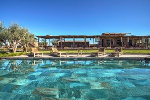 A clear pool with lounge chairs and a covered seating area.