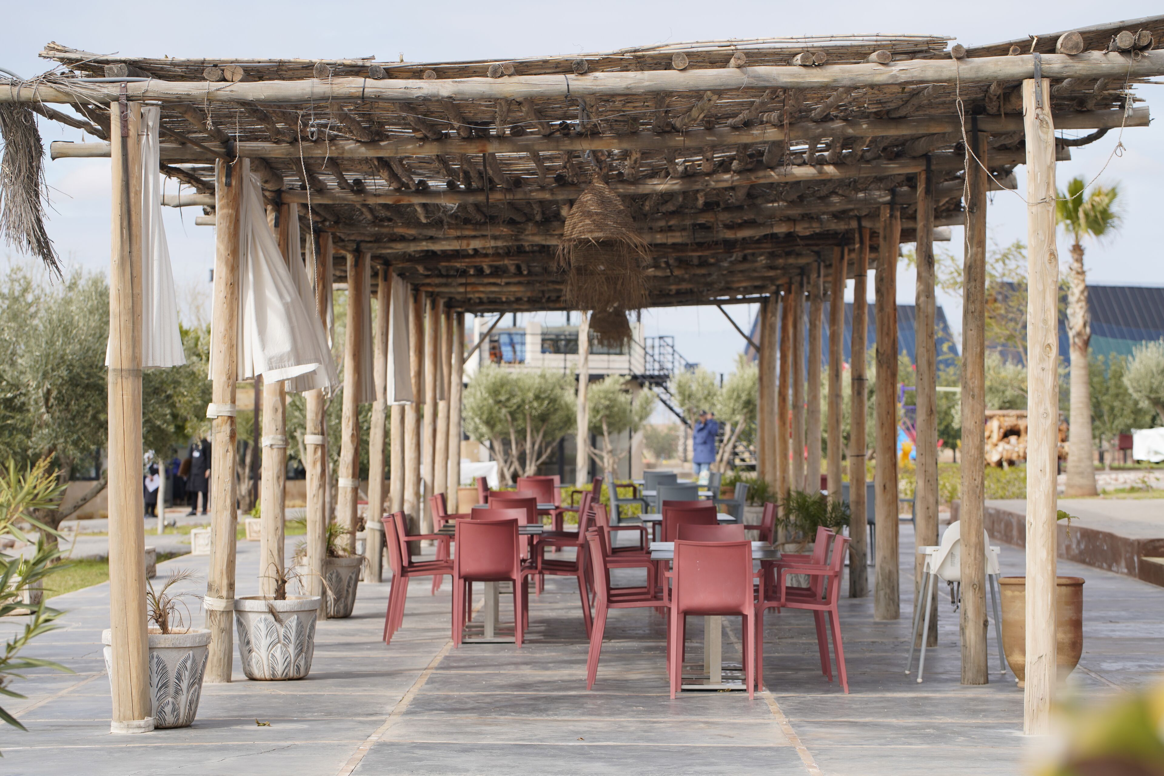 Un área de estar al aire libre con pérgola de madera, sillas rojas y plantas en macetas.