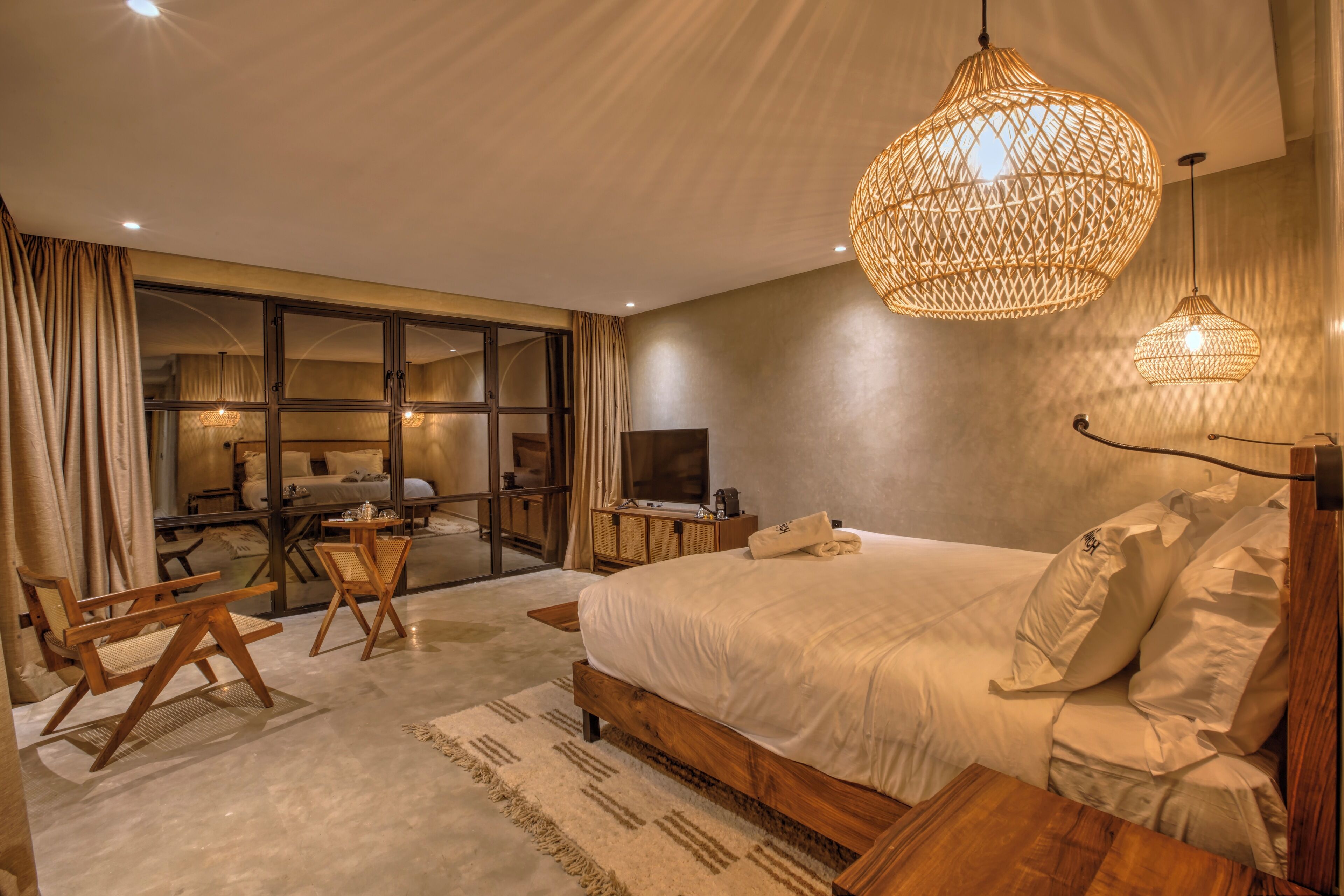 Un dormitorio moderno con una cama grande, muebles de madera, un televisor y un baño con paredes de vidrio.