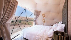 A bedroom with a large window, a bed, a bedside lamp, and a basket. - The Ranch resort (Aghouatim)