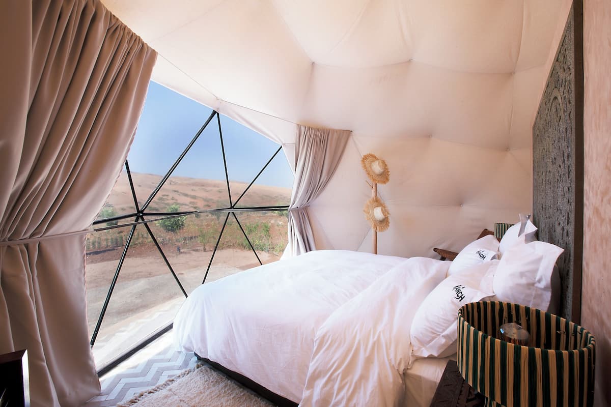 Ein Schlafzimmer mit großem Fenster, einem Bett, einer Nachttischlampe und einem Korb.