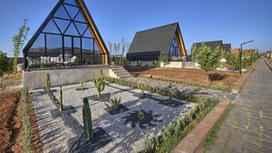 A modern building with a triangular glass facade and a sloped roof, surrounded by a landscaped garden with cacti and gravel paths. - The Ranch resort (Aghouatim)