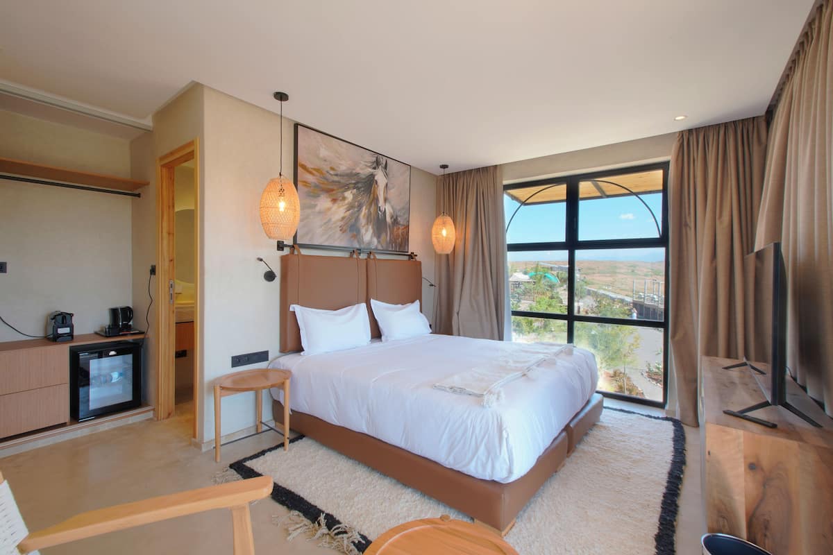 Ein modernes Hotelzimmer mit einem großen Bett, einem Schreibtisch, einem Fernseher und Blick ins Freie.