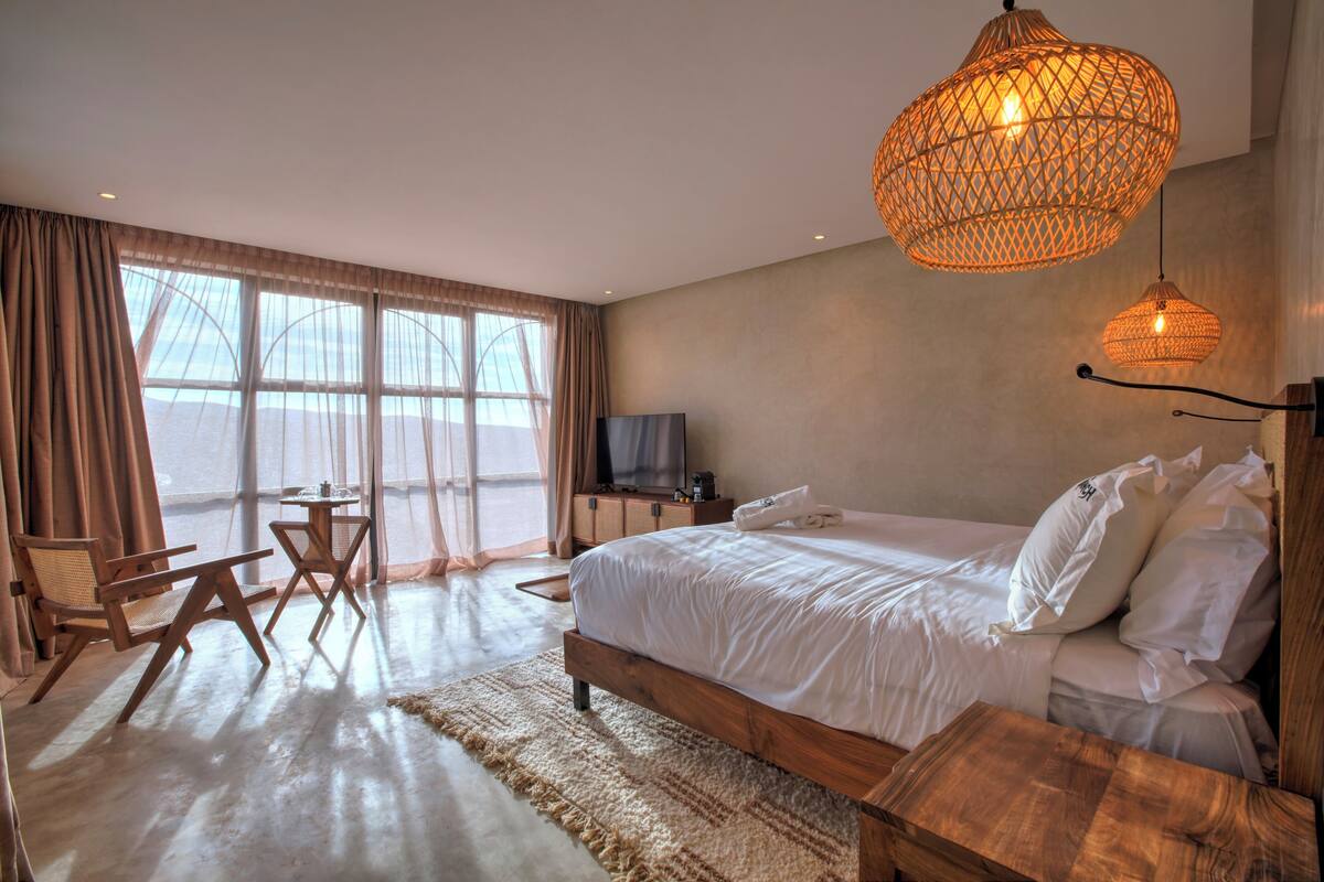 Ein Schlafzimmer mit einem großen Bett, Holzmöbeln, einem Fernseher und Blick durch große Fenster.