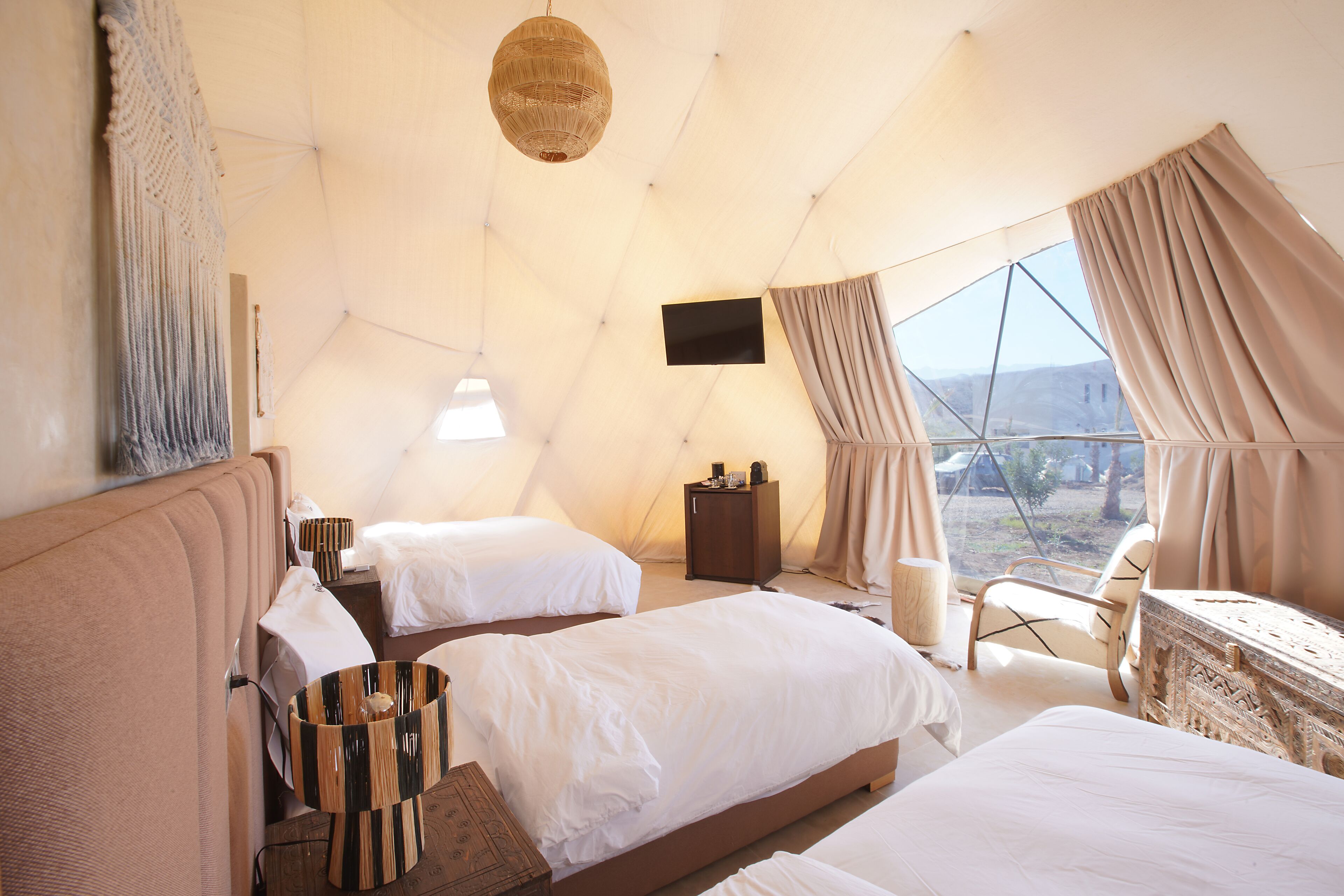 A tent-style room with two beds, a flat-screen TV, a wooden cabinet, and a view of the outdoors.