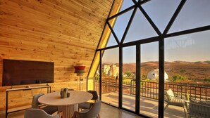 A modern interior with a large window, wooden ceiling, and a dining area with chairs and a table. - The Ranch resort (Aghouatim)
