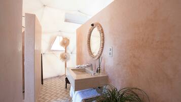 A bathroom with a marble sink, a round mirror, and a potted plant.