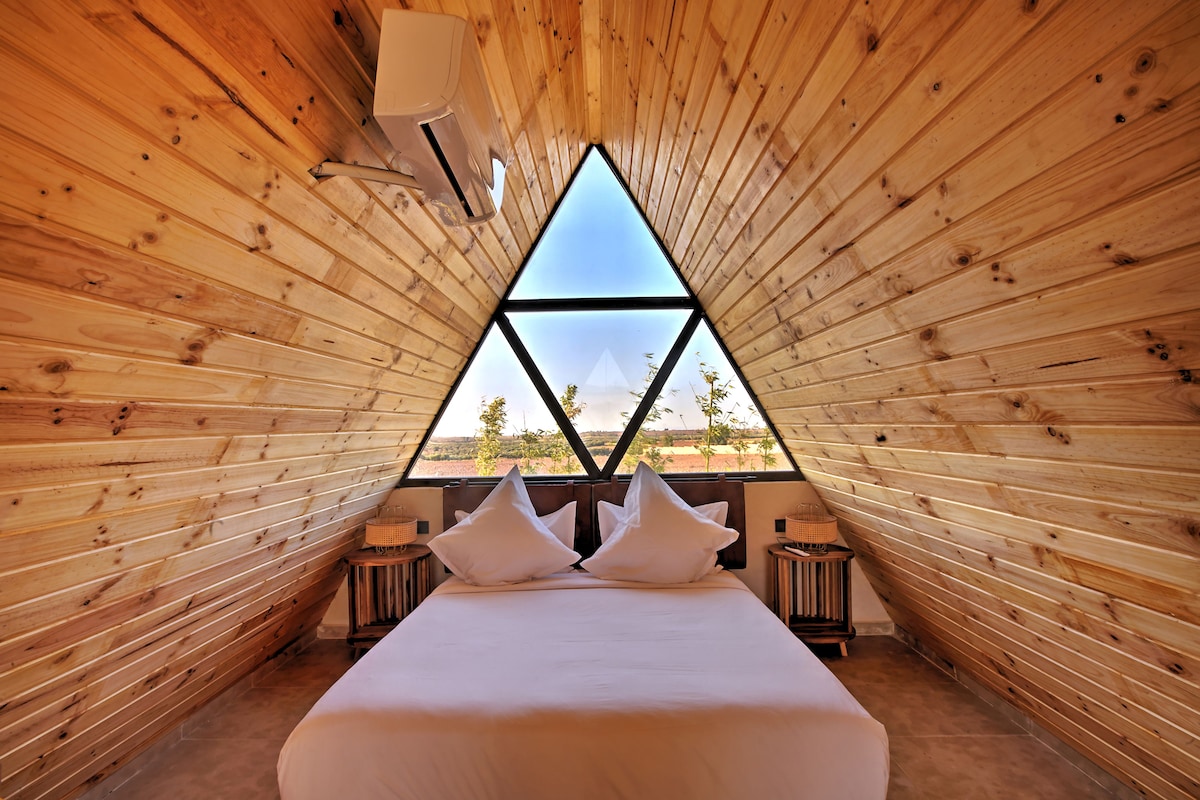 A triangular room with a bed, pillows, and a window.