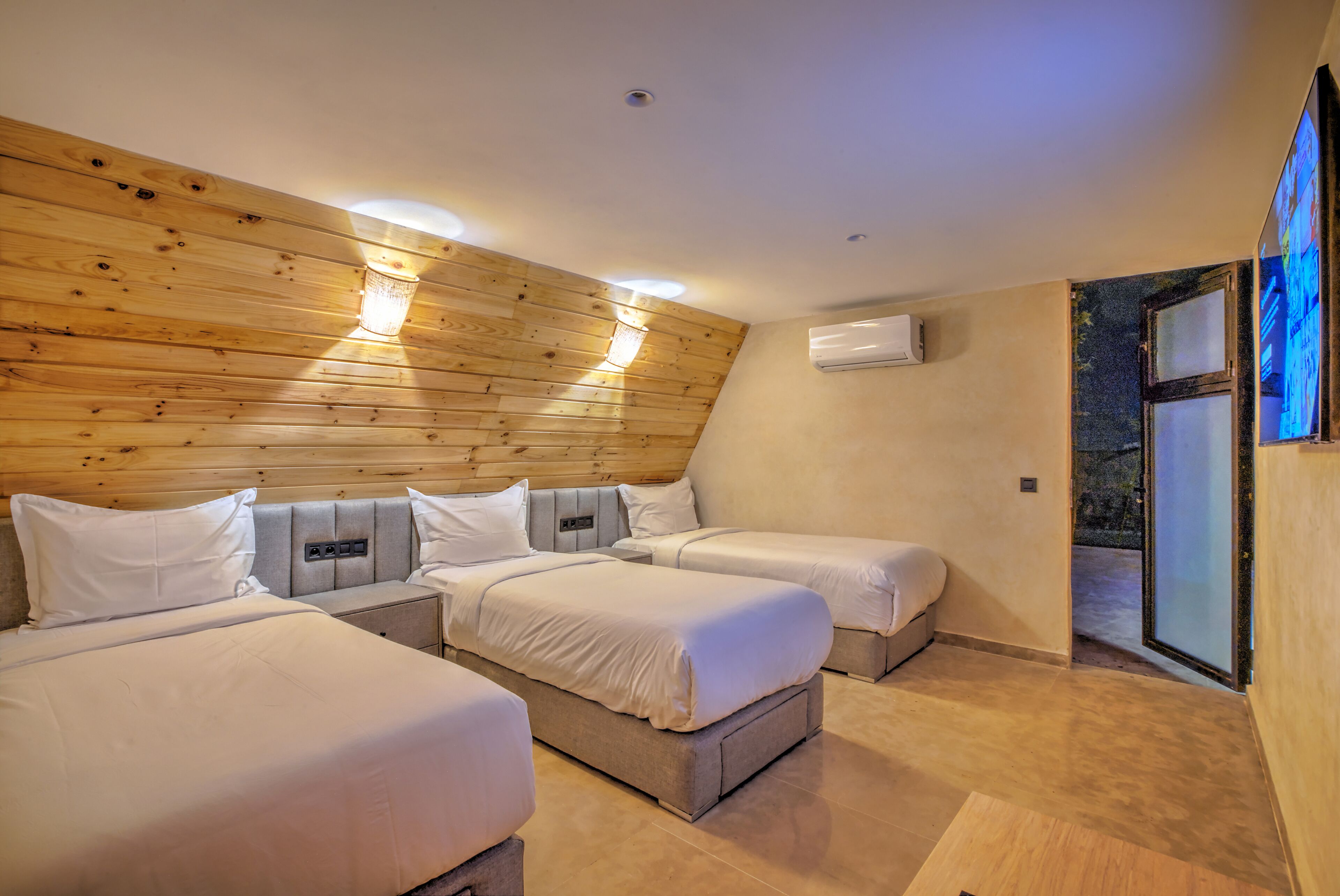 A room with three beds, wooden paneling on the walls, an air conditioning unit, and a sliding glass door.