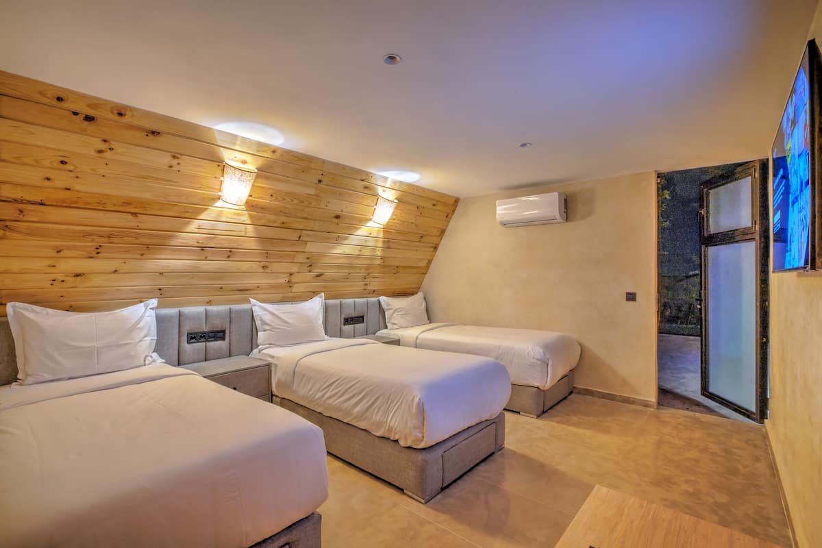 Ein Hotelzimmer mit drei Betten, Holzvertäfelung an den Wänden, einer Klimaanlage und einer Glasschiebetür zu einem Außenbereich.