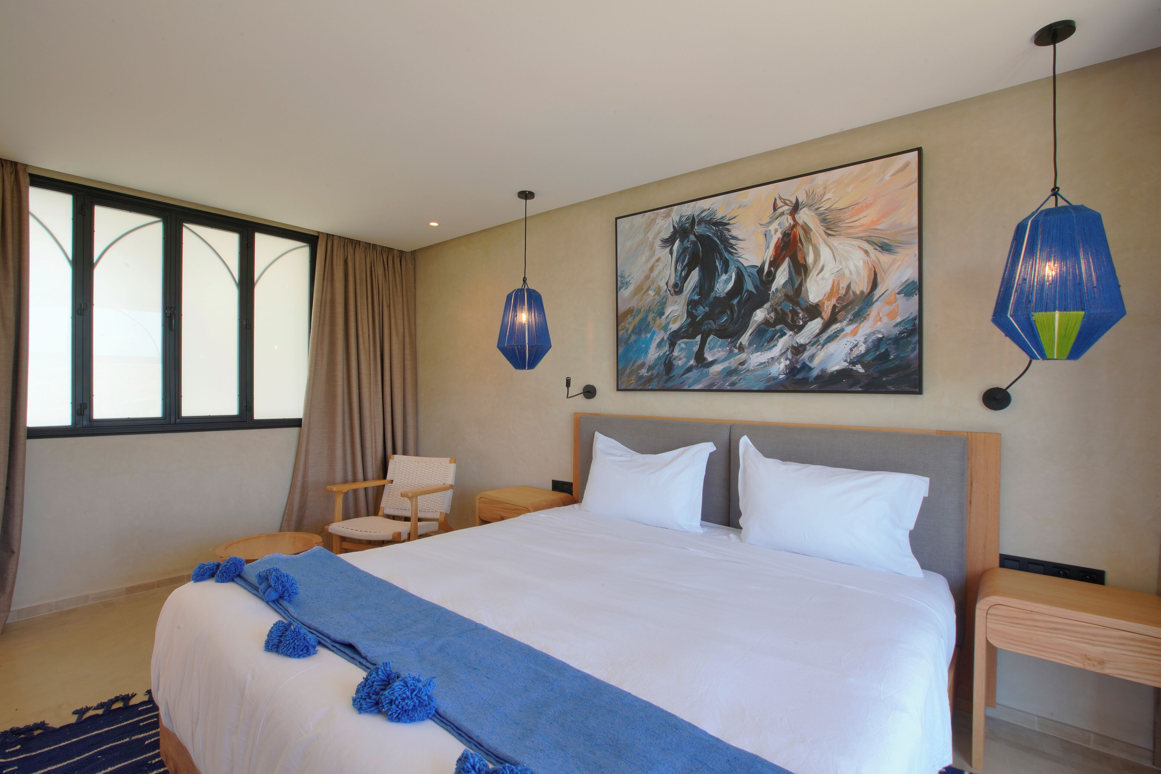 Habitación de hotel con una cama grande, un cuadro de un caballo y dos lámparas colgantes.
