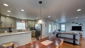 Una cocina moderna con una isla central, mesa de comedor de madera y luces empotradas en el techo.