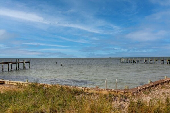 Paisaje costero con un muelle de madera que se adentra en aguas tranquilas, rodeado de zonas verdes.