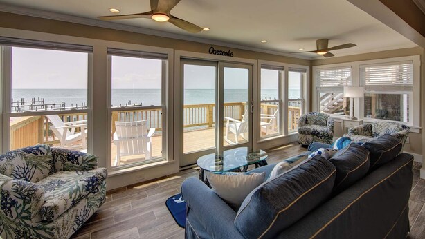 A spacious room with a large window overlooking the ocean, a ceiling fan, and a cozy seating area with a glass coffee table.