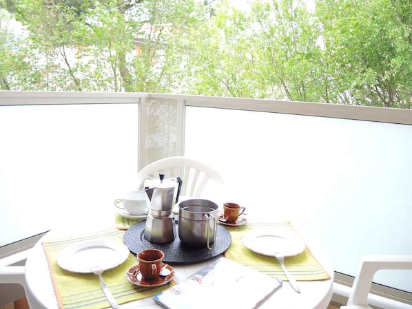 A dining table set with plates, cups, and a coffee maker on a balcony with a view of trees.