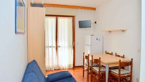 A small room with a bed, a table with chairs, a television, and a refrigerator. - Holiday apartment mit Terrasse (Bibione)