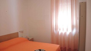 A hotel room with a bed, a small table with two cups, a door, and a window with curtains. - Holiday apartment mit Terrasse (Bibione)