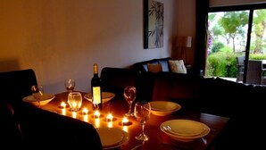 En svagt upplyst matplats med levande ljus, en vinflaska och utsikt över grönskan utanför.