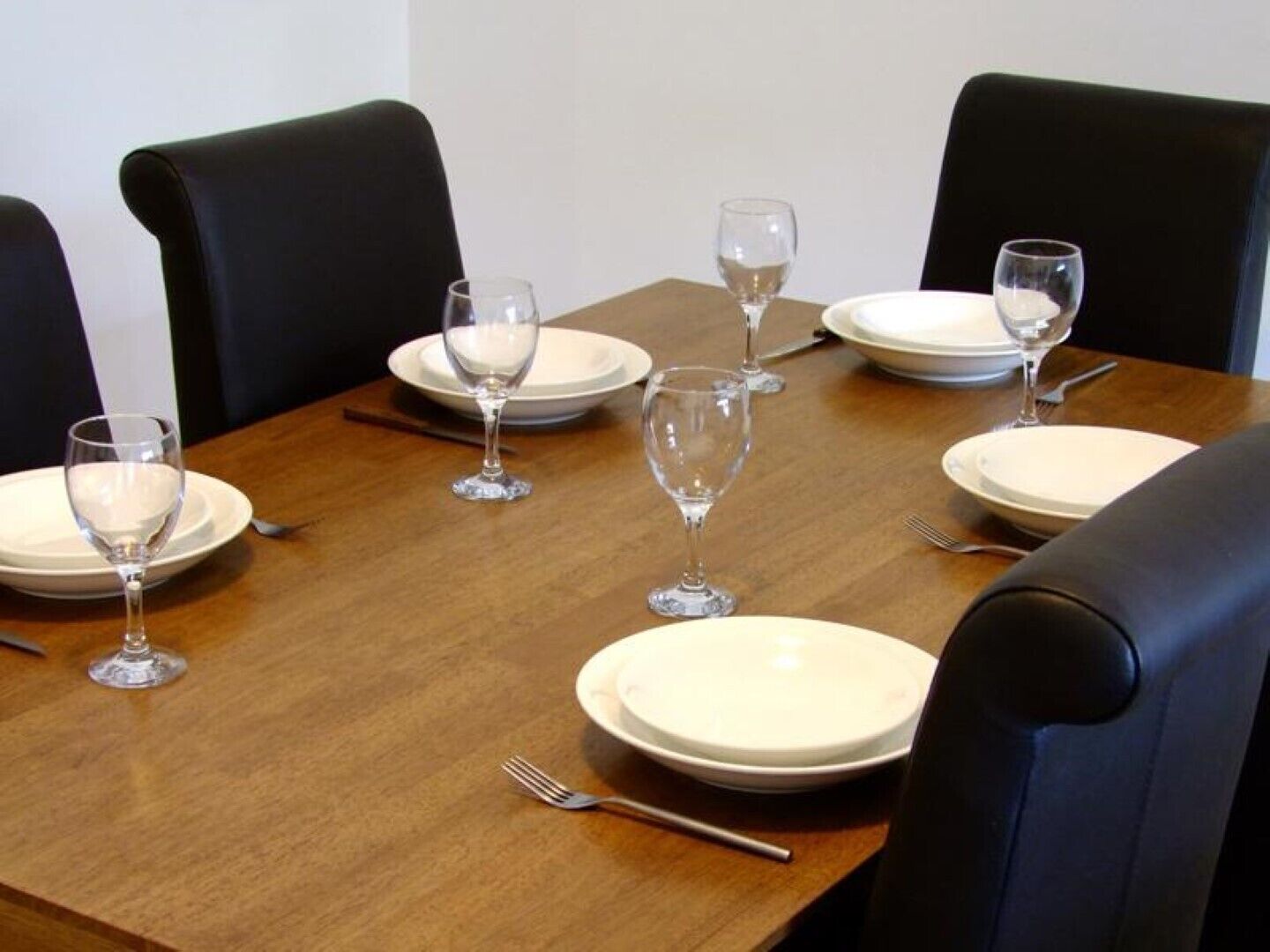 A dining table set with white plates, clear wine glasses, and silverware.