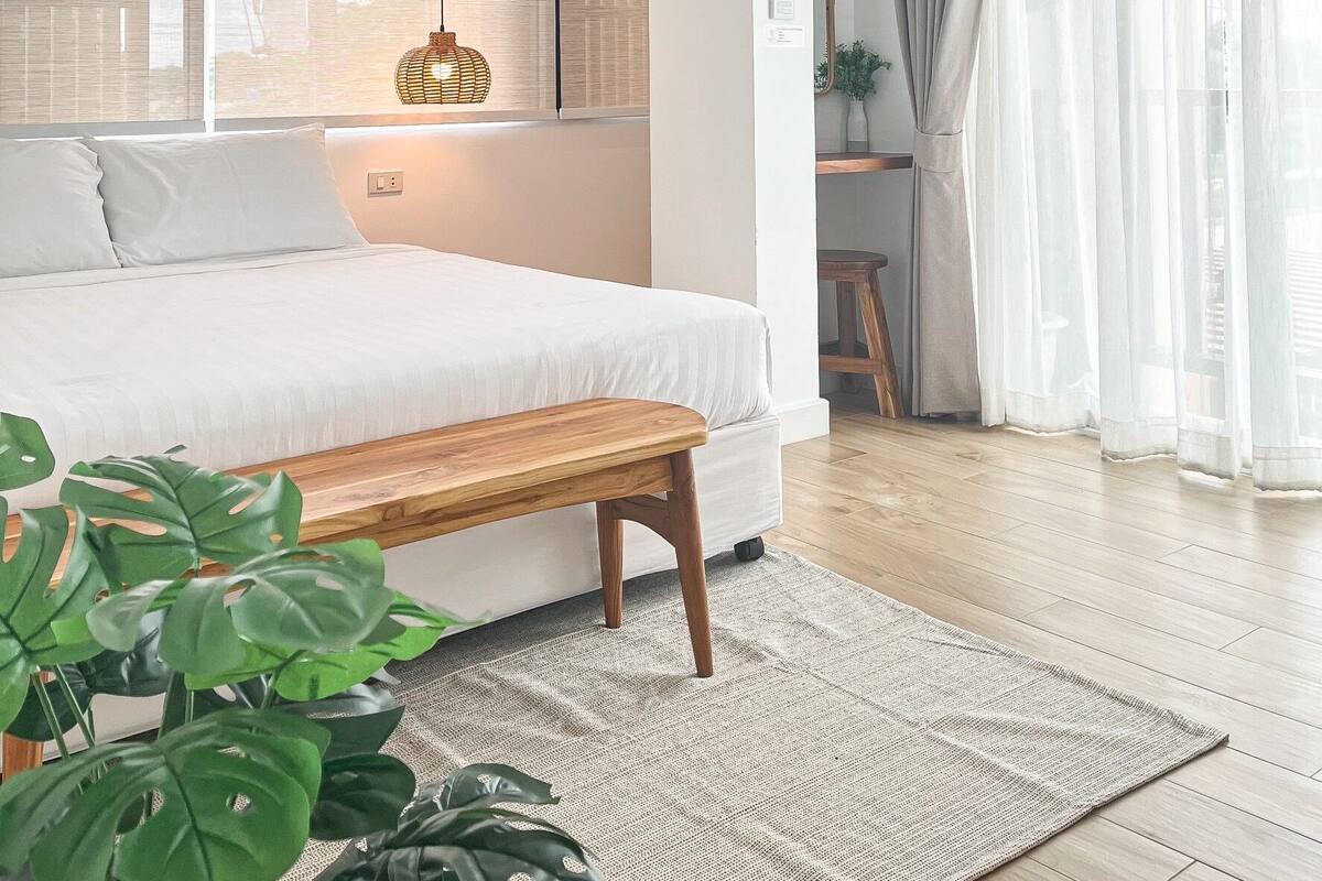 A bedroom with a bed, bench, potted plants, and a view of the outside.