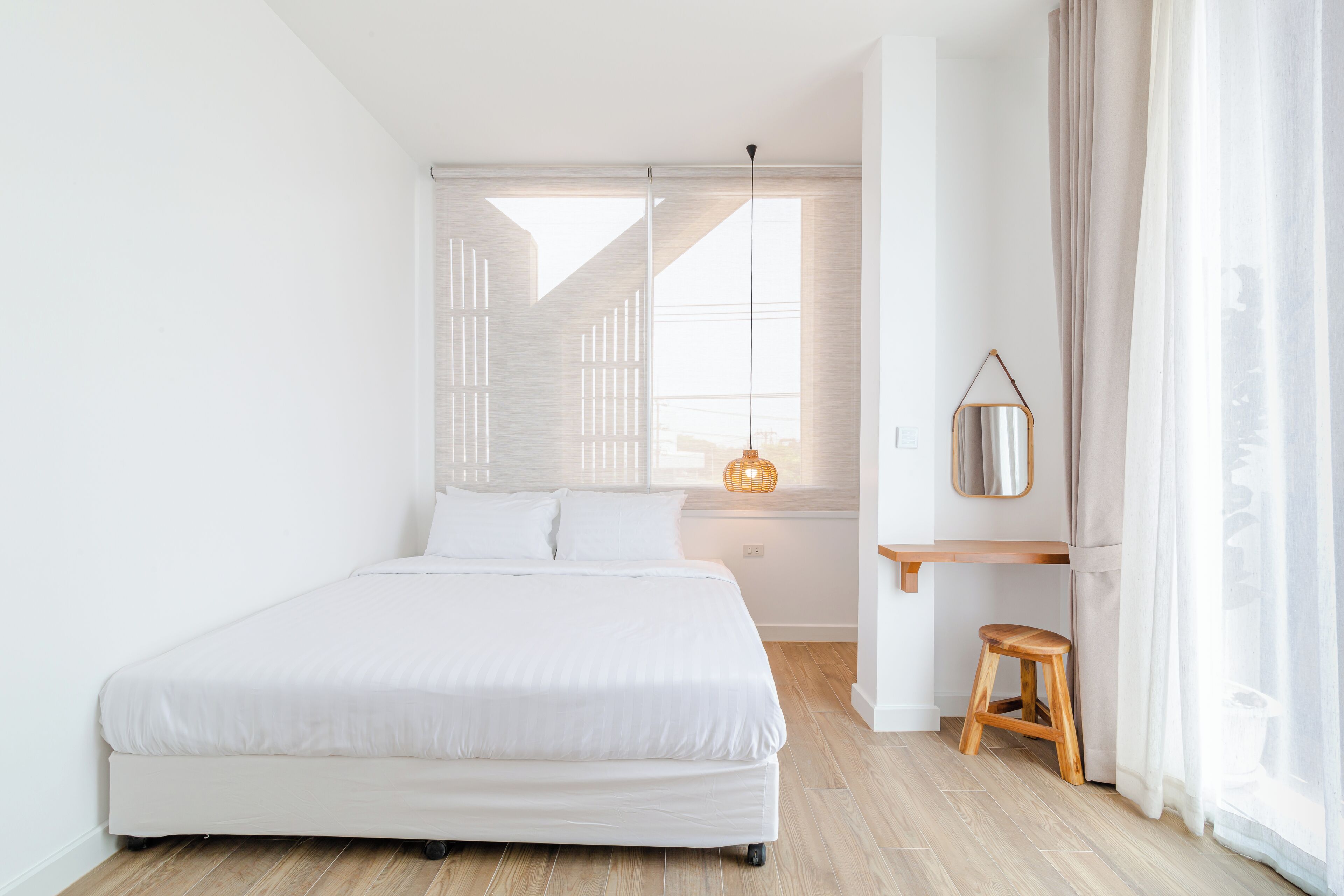 A modern bedroom with a large bed, a small stool, a bedside table, and a window with blinds.