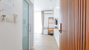 Habitació d'hotel moderna amb terra de fusta, una porta de vidre, un armari blanc, una cuineta petita i un televisor fixat a la paret.